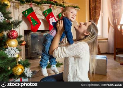 Young mother playing with her baby boy on floor at Christmas tree