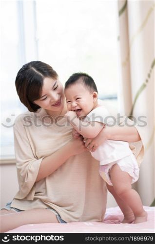 Young mother playing with her baby on the bed