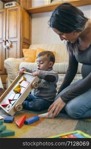 Young mother playing with her toddler son a wooden game building in the living room. Mother playing with toddler a wooden game building