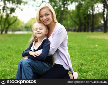 Young mother playing with little daughter in green summer park