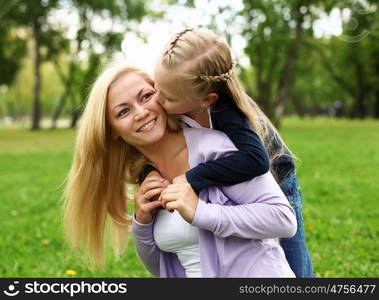 Young mother playing with little daughter in green summer park