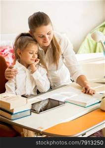 Young mother pointing in exercise book and explaining homework to daughter