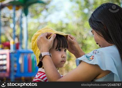 Young mother puts a hat on her daughter in the summer park. Family spends time together on vacation.