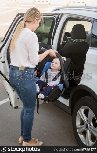 Young mother putting car seat with her baby boy in the car
