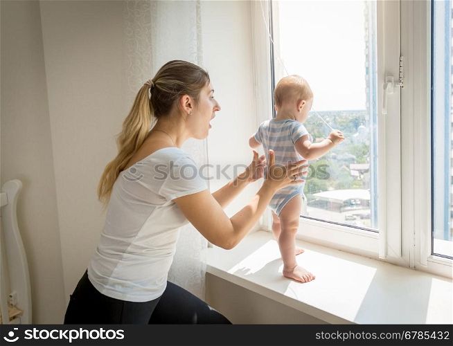Young mother rushing to her baby that is trying to open window