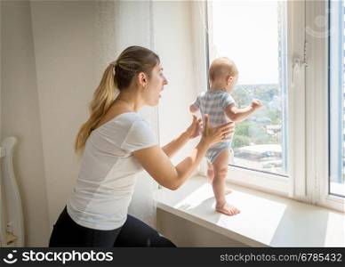 Young mother rushing to her baby that is trying to open window