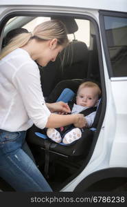 Young mother seating her baby in car safety seat