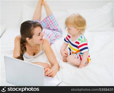 Young mother showing baby something in laptop