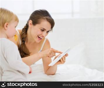 Young mother showing baby something in tablet PC