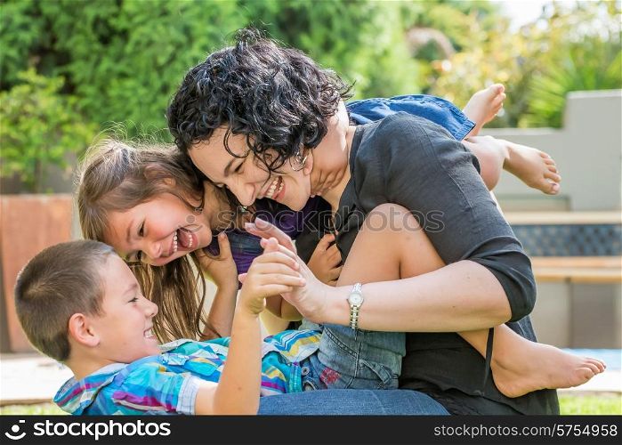 Young mother, son and daughter playing outside on the lawn in sunny weather, having fun, laughing with joy.