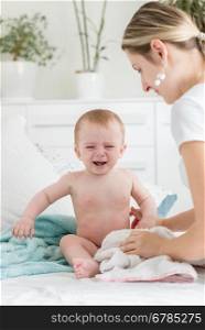 Young mother soothing her crying baby boy sitting on bed