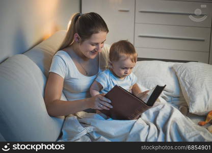 Young mother storytelling to her adorable baby boy at bed