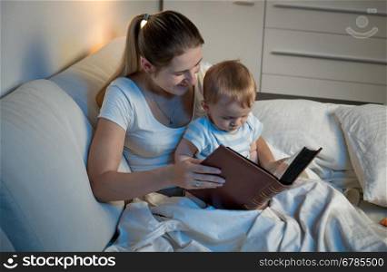 Young mother storytelling to her adorable baby boy at bed before going to sleep