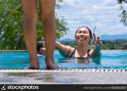 Young mother takes care of a daughter who is about to jump into the pool. Cute little girl having fun swimming with her mother in the pool on a sunny day. Summer lifestyle concept. focus on mom