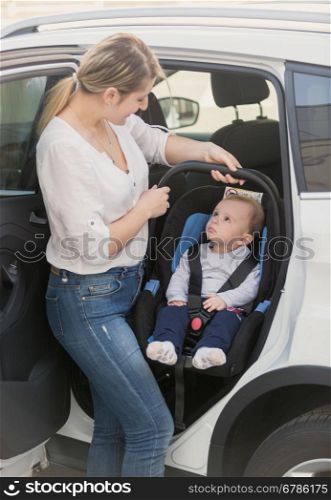 Young mother taking her baby in safety seat out of the car