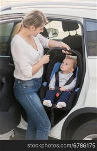 Young mother taking her baby in safety seat out of the car