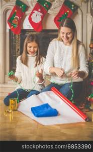 Young mother teaching her daughter how to wrap Christmas presents
