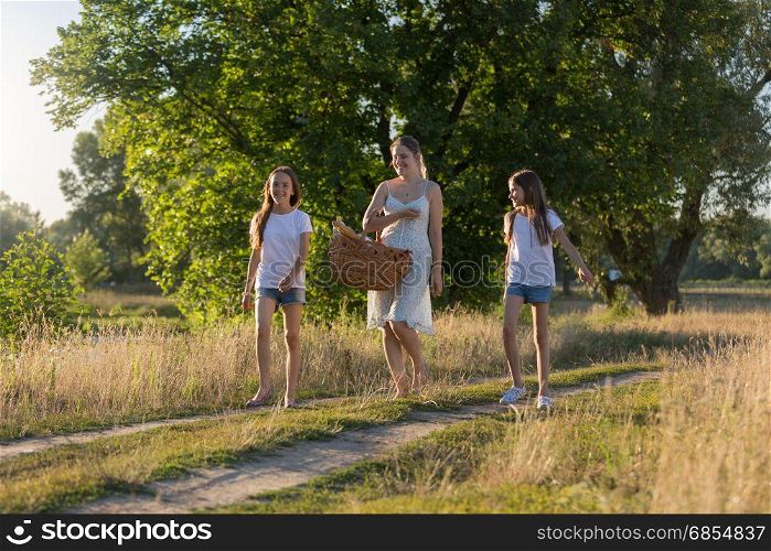 Young mother walking with her daughter in meadow at sunset