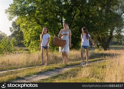 Young mother walking with her daughter in meadow at sunset