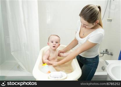 Young mother washing her baby son in bath