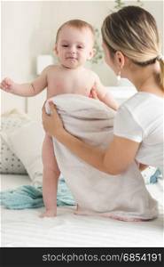 Young mother wiping her baby boy with towel on bed
