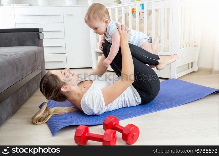 Young mother with baby doing yoga exercise on floor at living room