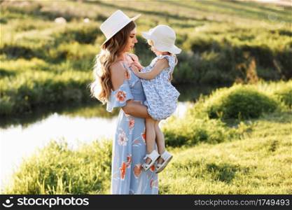 Young mother with baby girl near river background. Beautiful mum, little daughter outdoors. Portrait mom with child together walks in nature. Happy Mother’s Day. Young mother with baby girl near river background. Beautiful mum, little daughter outdoors. Portrait mom with child together walks in nature. Happy Mother’s Day.