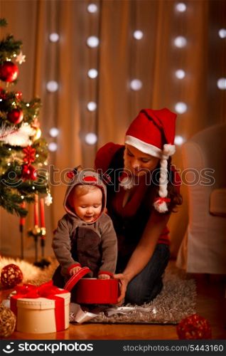 Young mother with happy baby opening present box near Christmas tree&#xA;