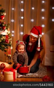 Young mother with happy baby opening present box near Christmas tree&#xA;