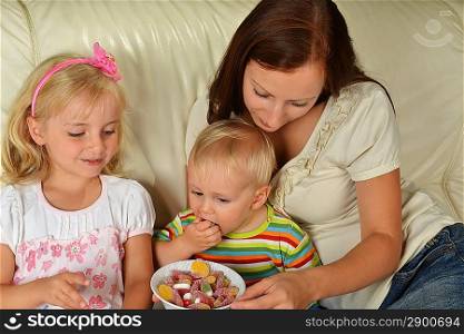 Young mother with her children at home eating candy