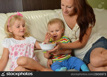 Young mother with her children at home eating candy