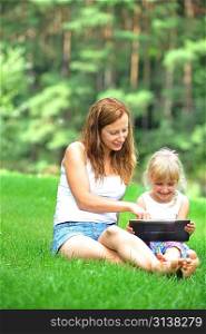 young mother with her daughter looking at screen of laptop. summer day.