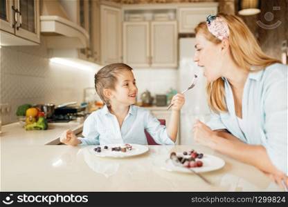 Young mother with her kid tastes chocolate pastry. Cute woman and little boy cooking on the kitchen. Happy family tasting sweet dessert at the counter and having fun. Mother with kid tasting dessert and having fun