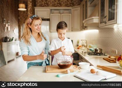 Young mother with her son mixing melted chocolate in a bowl. Cute woman and little boy cooking on the kitchen. Happy family prepares sweet dessert at the counter. Mother with son mixing melted chocolate in a bowl
