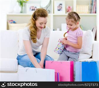 Young mother with little daughter openning shopping bags of gifts at home