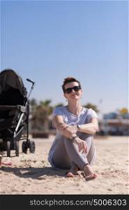 Young mother with sunglasses relaxing on beach with baby stroller outdoor