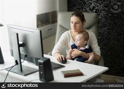 Young mother working at home office and taking care of her baby son