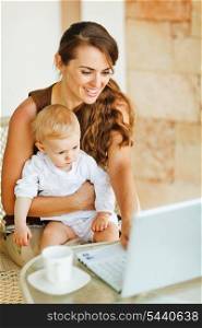 Young mother working with baby on laptop