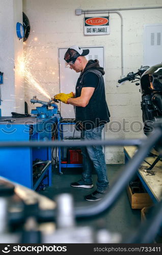 Young motorcycle mechanic using a grinder in the workshop. Motorcycle mechanic using a grinder