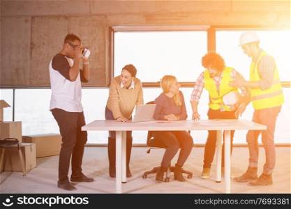 young multiethnic business team checking documents and business workflow on construction site using the virtual reality headset and laptop computer with sunlight through the windows during moving in at new startup office