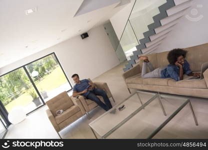 Young multiethnic couple relaxes in the luxury living room, using a tablet and laptop computer