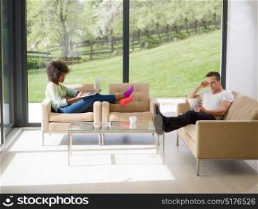 Young multiethnic couple relaxing at luxurious home with laptop computers reading in the living room on the sofa couch.