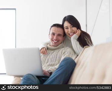 Young multiethnic couple relaxing at luxury home using laptop computer reading in the living room on the sofa couch.