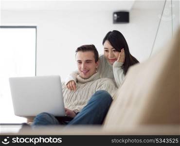 Young multiethnic couple relaxing at luxury home using laptop computer reading in the living room on the sofa couch.