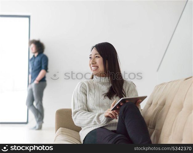 Young multiethnic couple relaxing at luxury home with tablet computers reading in the living room on the sofa couch.
