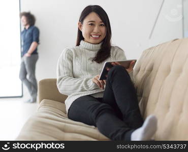 Young multiethnic couple relaxing at luxury home with tablet computers reading in the living room on the sofa couch.