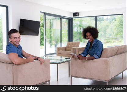 Young multiethnic couple sitting on a sofa in the luxury living room, using a tablet computer