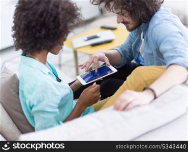 Young multiethnic couple sitting on a sofa in the luxury living room, using a tablet computer