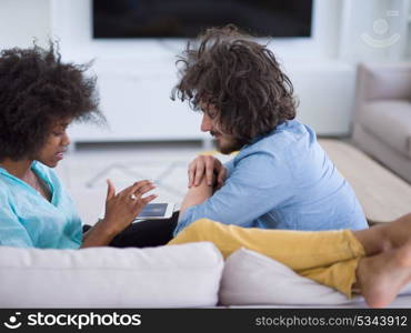 Young multiethnic couple sitting on a sofa in the luxury living room, using a tablet computer