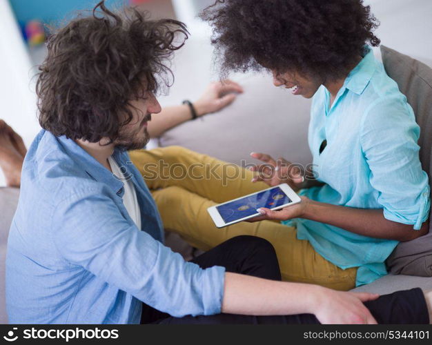 Young multiethnic couple sitting on a sofa in the luxury living room, using a tablet computer